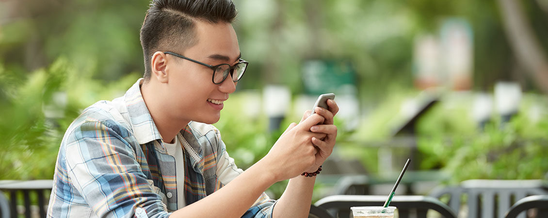 vestido-casualmente-jovem-asiático-homem-sentado-ao-ar-livre-café-usando-smartphone